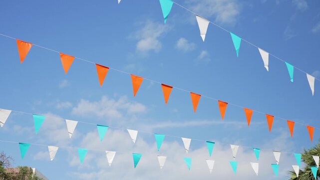 Colorful triangular flags hanging outdoors against blue sky, creating a cheerful decoration for kids birthday party, family celebration, or playful outdoor event.