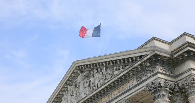 Paris&mdash;French flag waving atop a grand neoclassical facade with sculpted pediment and columns. Elegant government architecture under blue sky
