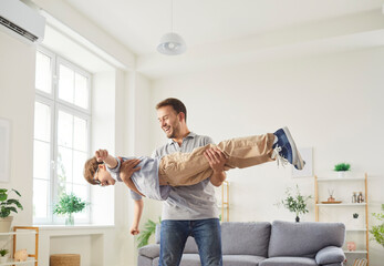 Happy loving family father and son having fun in living room together, playing flying plane. Joyful young dad spinning around laughing little boy, holding child while kid putting up arms like plane.