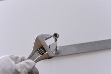 Adjustable wrench tightening nut on steel bar with gloved hand