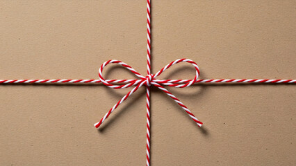 Close-up of red and white baker's twine tied in a bow on a brown cardboard background, gift wrapping concept