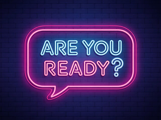 Are you ready? the blue and pink neon text sign glows brightly on a dark brick wall background