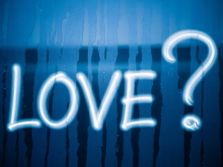 A glowing question mark next to the word love written on a blue foggy window pane