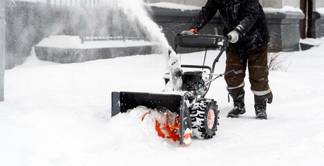 A man with a snow blower removes snow in the yard of a house