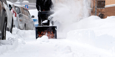 A man with a snow blower removes snow in the yard of a house