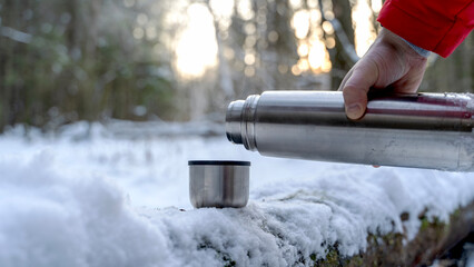 A man pours hot tea or a thermos in a winter forest