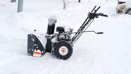 A man with a snow blower removes snow in the yard of a house