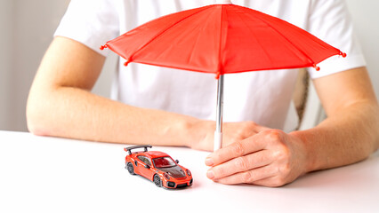 An insurance agent holds an umbrella over a car model. Car insurance concept