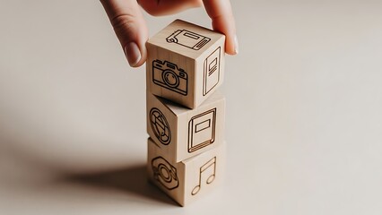 A hand stacking wooden blocks with various symbols on a plain background