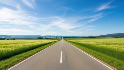 Fototapeta premium Empty road through green fields under a blue sky with clouds