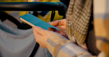 Woman while strolling through scenic park, pushing baby stroller and browsing smartphone during leisurely autumn afternoon