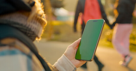 Woman holding a smartphone with a green screen for copy space, isolated on green background