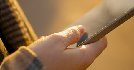 Woman swiping smartphone screen while standing in park, engaging with mobile technology and digital content during outdoor leisure moment