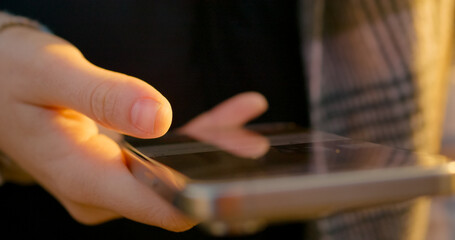 Female swiping smartphone screen during golden sunset light. Fingers scrolling wireless digital...