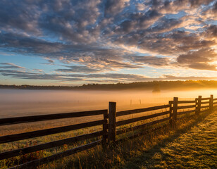 Serene sunrise over foggy field with rustic wooden fence