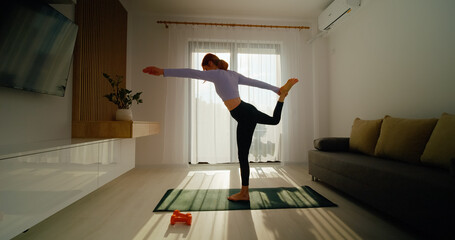 In a bright living room, a woman focuses on yoga and stretching exercises for improved balance and flexibility. Morning sunlight fills the space, enhancing her practice.