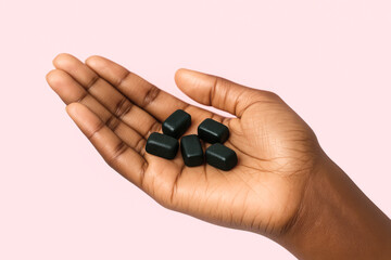 person's hand displaying a handful of dark green rectangular vitamin gummies representing health wellness and self-care on a light pink background