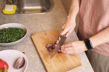 Woman slicing marinated meat on a wooden cutting board next to bowls of chopped red pepper, red onion, and green beans, preparing ingredients for a hearty hot dish