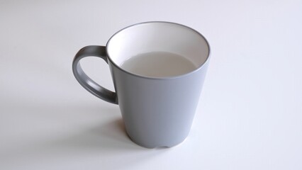 A grey ceramic mug with water stands on a white table, side and top view. Fresh water as a morning ritual. One object in the center of frame close-up. Minimalistic tableware. High quality photo.