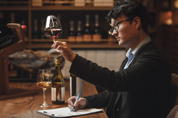 Asian Ethnicity Professional Sommelier Tasting Red Wine in Wine Cellar, Close up Photo. Alcoholic Beverages Degustation. Winemaking School, Wine Waiter Certification.
