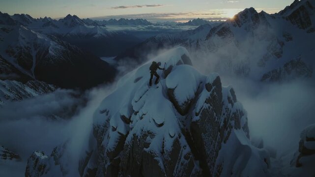 Man climbing on snowy mountain peak during sunset with ice axe and rope by rugged mountains