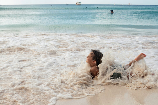 toddler on shore of beach as wave washes over him