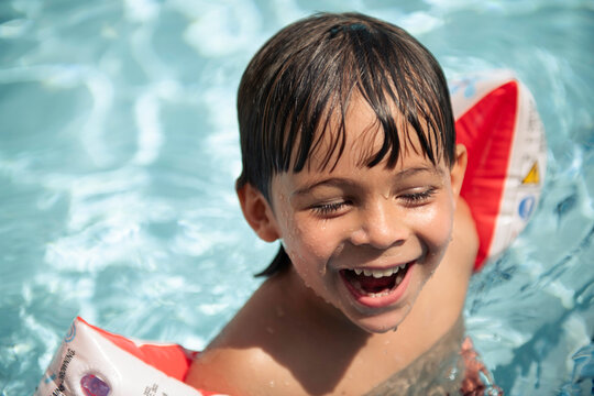 Young boy happily smiling in pool with water wings on