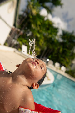 Young boy spouting water from his mouth at pool on sunny day