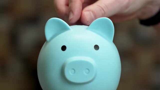 A person deposits coins into a cheerful blue piggy bank. This activity emphasizes the importance of saving and making smart choices with home finances. Every penny counts toward financial goals.
