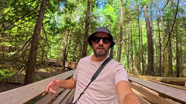 Happy tourist vlogging his experience while walking on a wooden pathway in the middle of a giant trees forest in cathedral grove nature park, british columbia