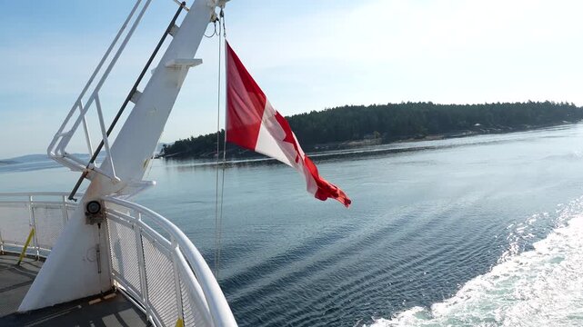 Canadian flag waving in the wind on a ferry sailing from vancouver island to vancouver, british columbia, canada, with the wake visible behind the ship