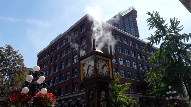 White steam rises from the gastown steam clock, a historic landmark in vancouver, british columbia, against a backdrop of a clear blue sky and a red brick building