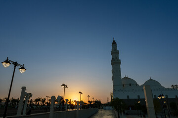 Obraz premium Quba mosque with a tall minaret against a clear sky with a sunset or sunrise glow, featuring illuminated streetlights.