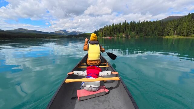 Family enjoying a peaceful canoe ride on maligne lake, surrounded by the stunning scenery of jasper national park in the canadian rockies, with a father paddling and his son relaxing in the front