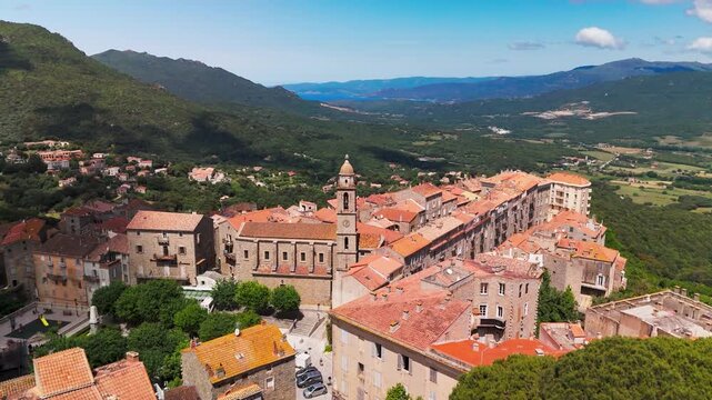 Smooth Cinematic Aerial Pull Back Shot Flying Out Over Sartene Medieval Town Towards Lush Green Valley and Forest Covered Mountains in Corsica, France.