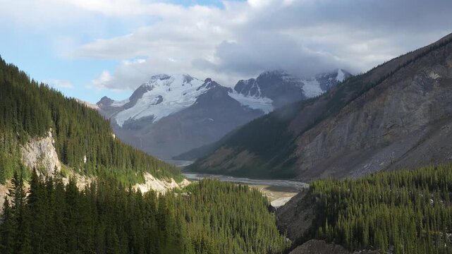 Majestic snow capped mountains and winding river cutting through lush pine valley, viewed from columbia icefield skywalk in canadian rockies