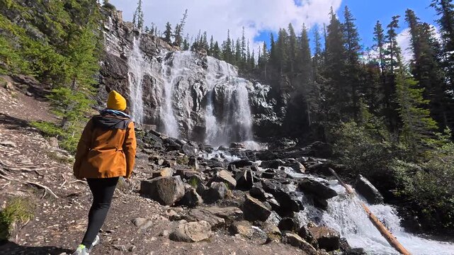 Majestic tangle creek waterfall attracts a female hiker exploring the natural beauty of banff national park in the canadian rockies, alberta, canada, during a sunny day