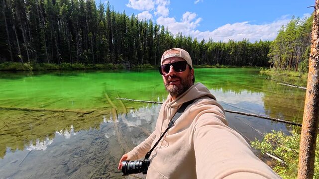 Turquoise waters of herbert lake reflect surrounding forest and sky as photographer gestures towards scenic beauty in banff national park, canadian rockies