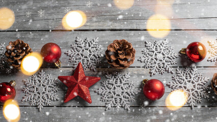 Christmas decorations including red ornaments, pinecones, snowflakes, and glowing lights arranged on a wooden surface