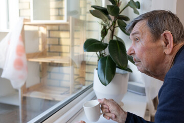 Senior male with beverage looking outside calm mood domestic setting side view.