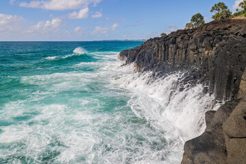 Water from a wave that broke on a steep basalt cliff flows slowly off the hexagonal column volcanic rocks into the rough waters at the base of the cliff at Fingal Head in New South Wales, Australia.