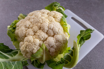 Fresh organic cauliflower with green leaves on white cutting board