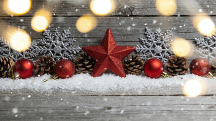 Christmas decorations including red ornaments, pinecones, snowflakes, and a red star on a snowy wooden background with bokeh lights