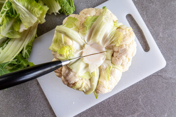 Fresh organic cauliflower with knife on cutting board, gray background