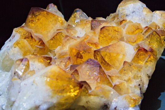 Macro photo of a golden yellow citrine quartz crystal cluster on a dark background, highlighting natural facets and sparkling texture.