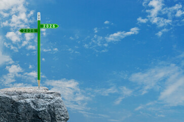 2026 and 2025 direction sign plate with green pencil on rock mountain over blue sky with white clouds, Business strategy and planning concept, Happy new year 2026 education cover
