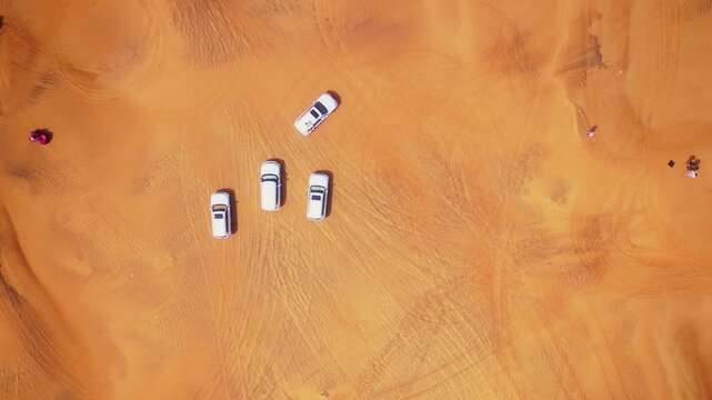 Top-down drone view of SUVs and desert tracks forming patterns in Dubai sand.