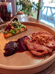 Gourmet roasted pork steak served with crispy onions, sauce and vegetable garnish on elegant plate in modern restaurant. Fine dining meat entr&eacute;e, European cuisine, food photography with shallow depth