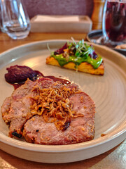 Gourmet roasted pork steak served with crispy onions, sauce and vegetable garnish on elegant plate in modern restaurant. Fine dining meat entr&eacute;e, European cuisine, food photography with shallow depth 