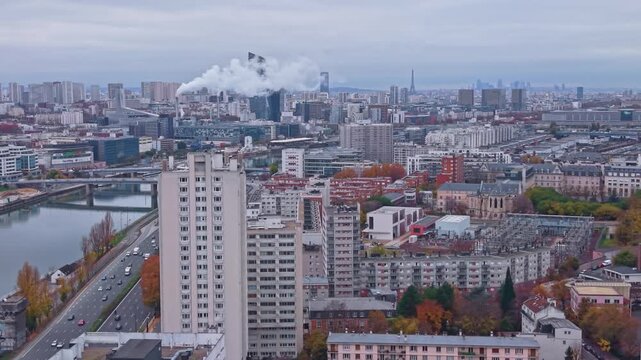 Aerial drone view of Paris suburbs with Ivry incinerator smoke and P&eacute;riph&eacute;rique highway traffic. Urban skyline featuring high-rise buildings and a distant Eiffel Tower in autumn, France